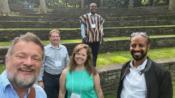 Five people smiling at the camera while standing on tiered steps with grass and stone.
